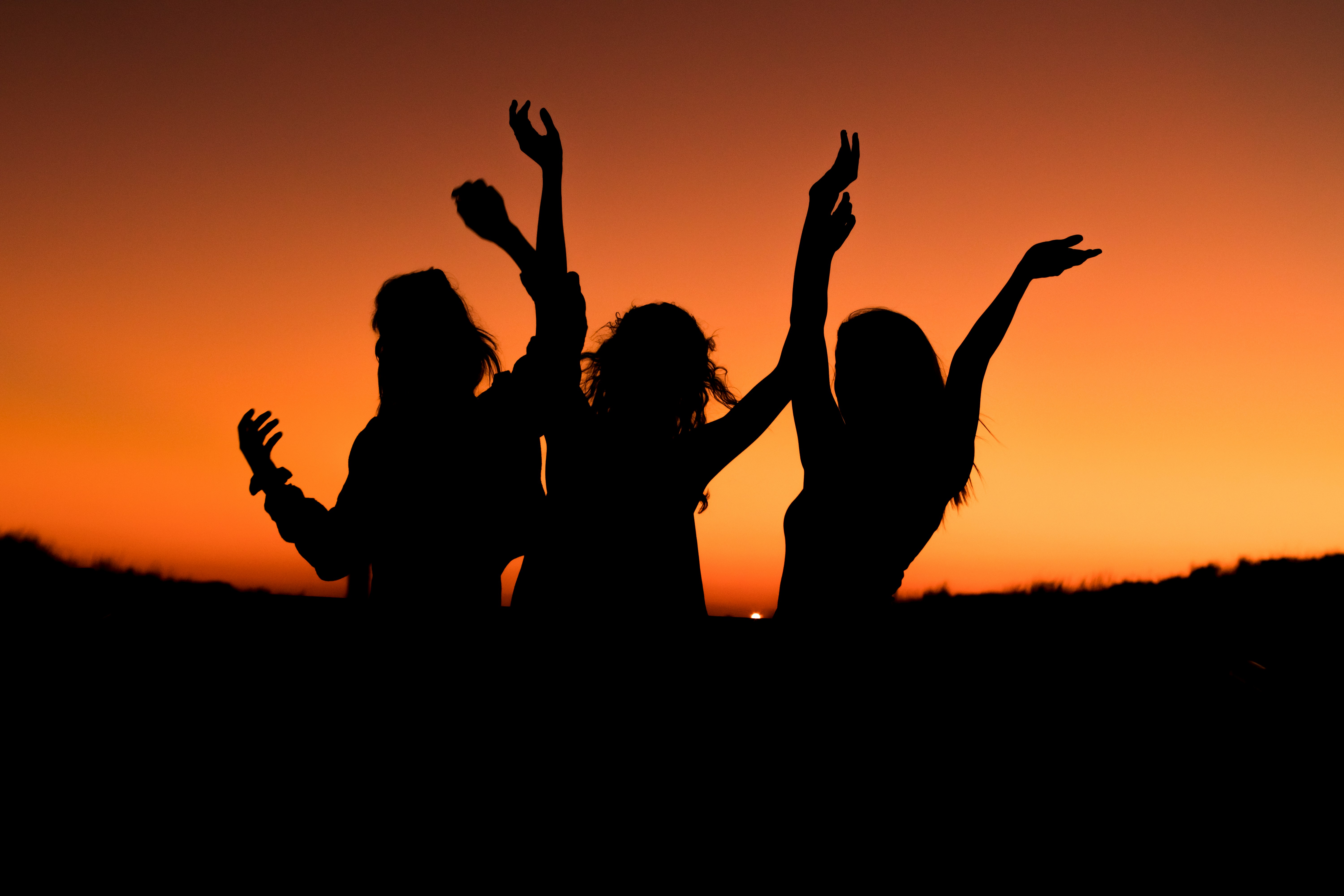 Silhouettes of ppl with hands in the air against a deep orange background.